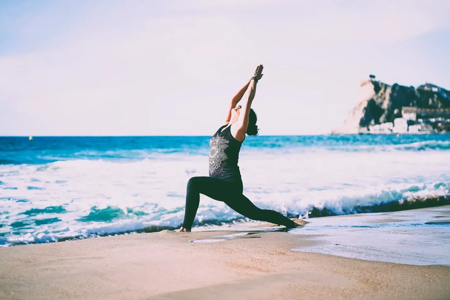 Kobieta na plaży w Hiszpanii z morzem w tle wykonująca pozycję jogi. Wyjazd dla kobiet - odkryj swoją moc